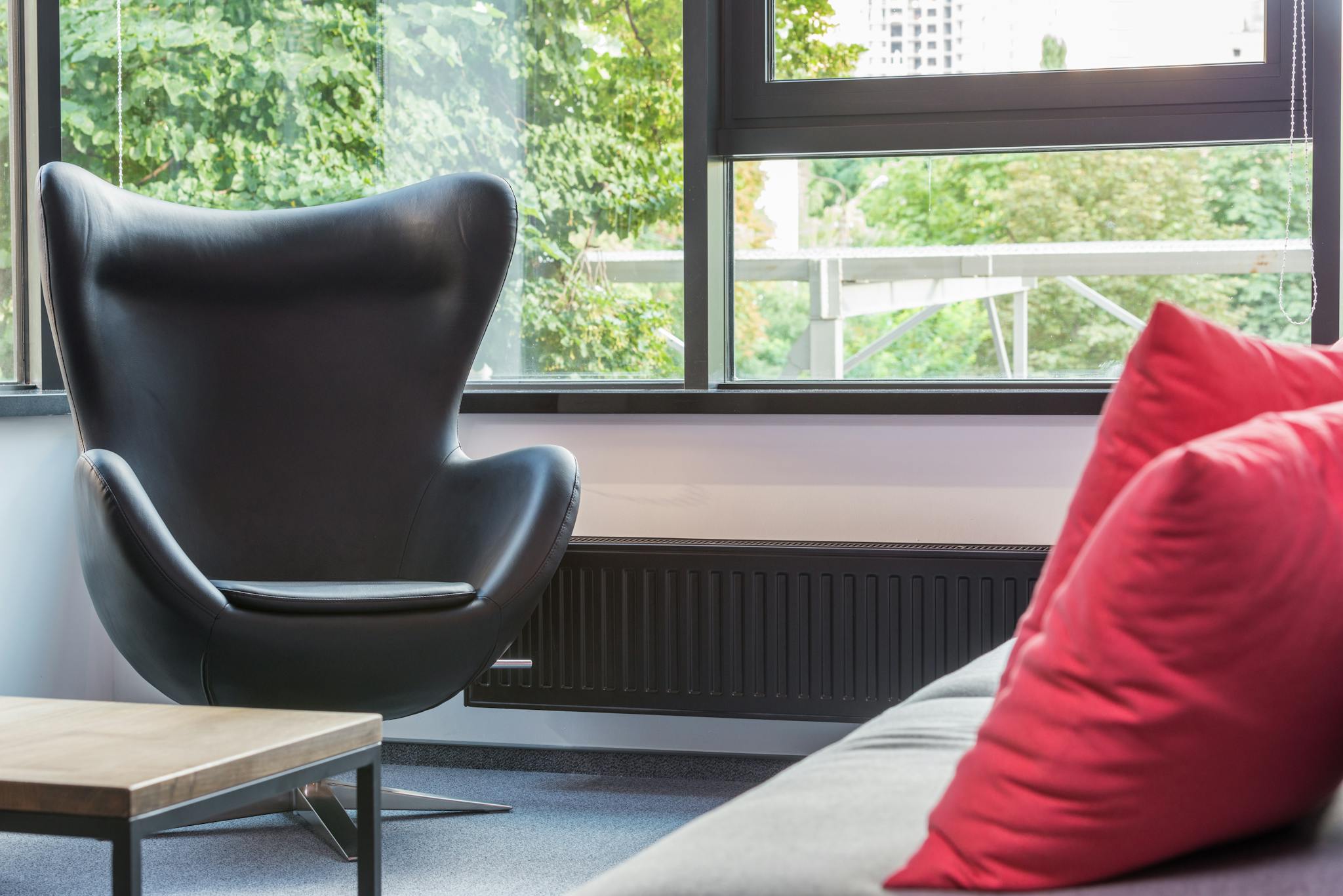 Bright and stylish modern living room featuring a black armchair, large window, and cozy red cushions on the couch.